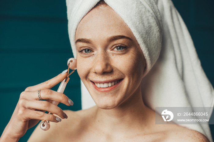 Close-up portrait of a woman getting massage face using jade facial roller for skin care. Facial tre