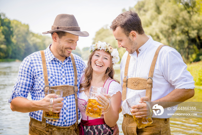 Freunde in bayerischen Tracht feiern an der Isar und trinken Bier. Oktoberfest München