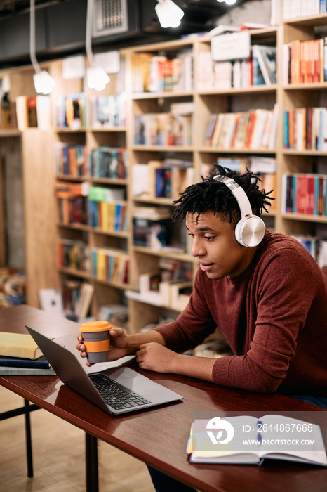 African American student uses laptop while drinking coffee and learning at university library.