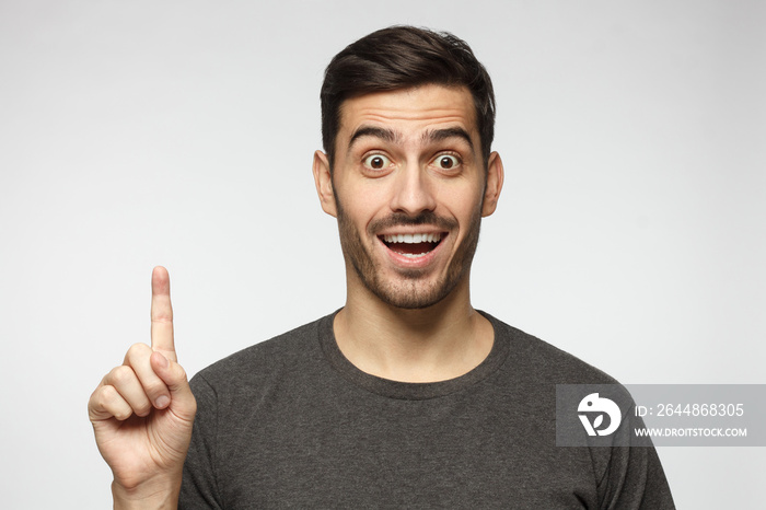 Portrait of excited young man looking at camera, smiling, pointing finger up if he has a great idea