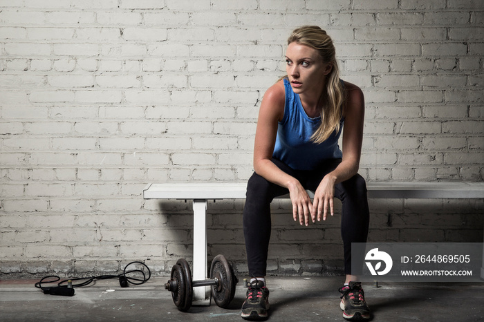 Woman looking away while relaxing on bench in gym