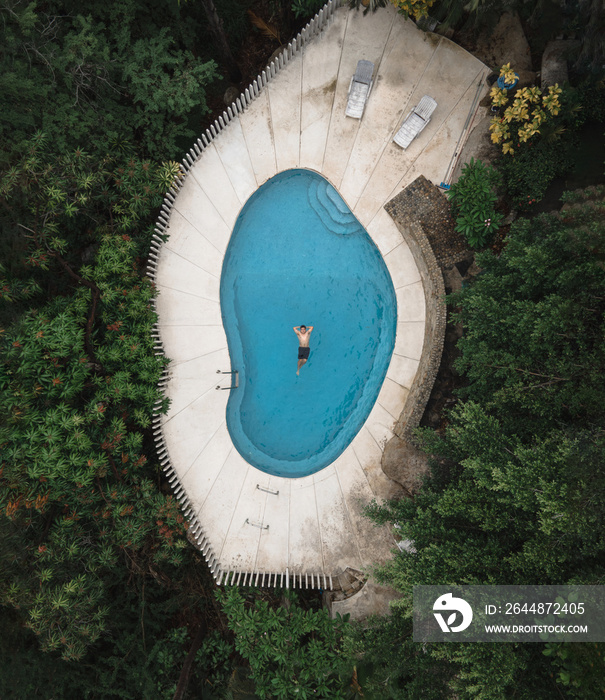 shot from a drone of a man swimming in the pool while on vacation