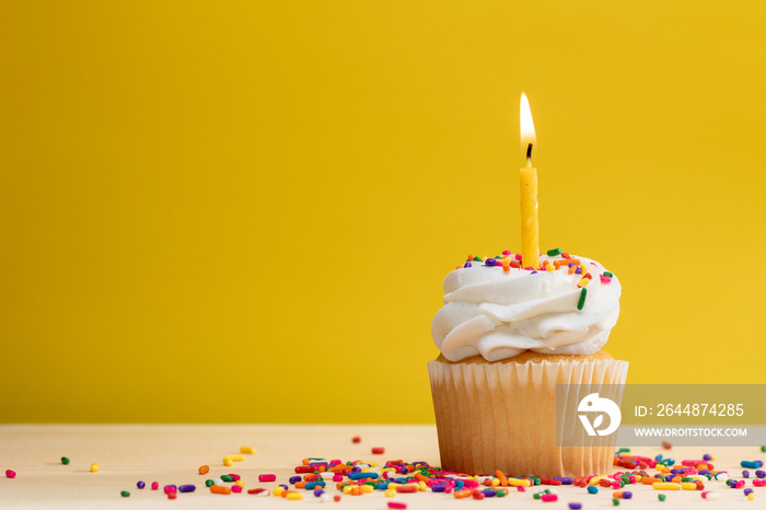 Yellow Cupcake with candle and sprinkles on a yellow background, with room for text