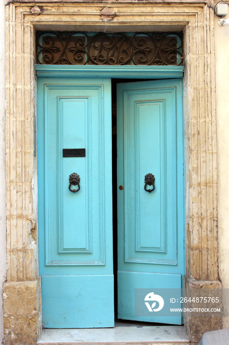 Turquoise blue doors, slightly ajar, with black iron metalwork knocker and letterbox, and limestone 