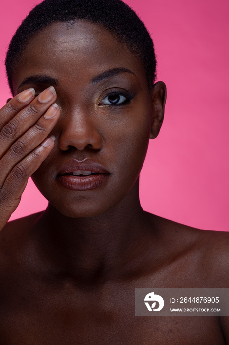 Studio portrait of shirtless woman touching eye against pink background