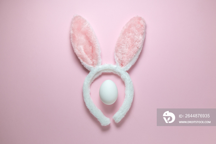 兔子耳朵复活节节日配饰和纯粉色背景上的白色鸡蛋的高角度视图。