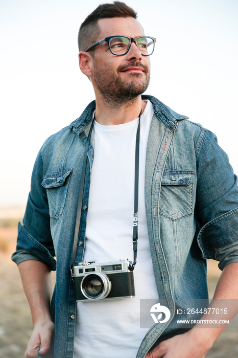 Hombre joven y sonriente con cámara de fotos analógica en medio de un desierto