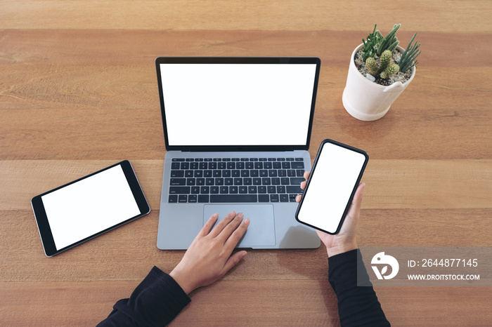 Top view mockup image of a hands holding a blank white screen mobile phone and laptop with black tab