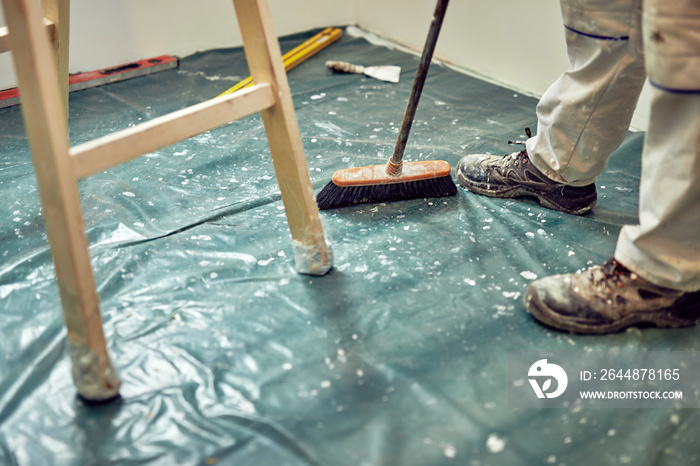 Worker using broom for cleaning dirt during renovaton of the house.