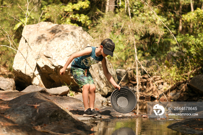 Young boy using pan to search for gold in creek, rural Australia