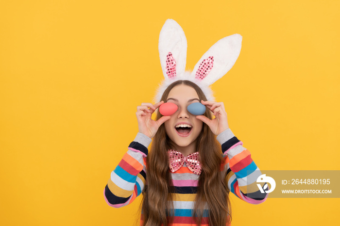 glad girl in bunny ears and bow tie hold easter eggs on yellow background