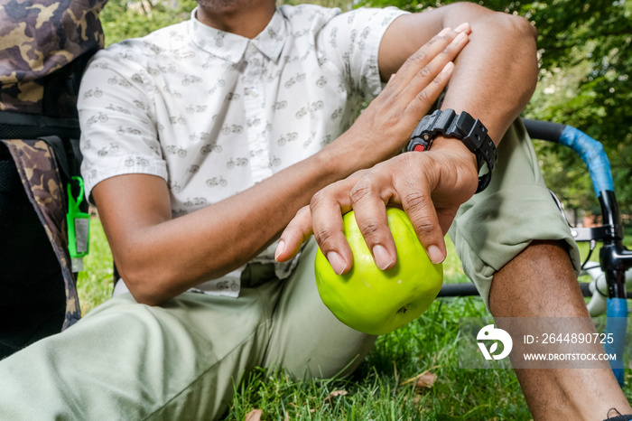 Close-up of man sitting on grass, holding apple