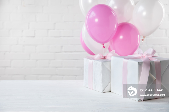 摆在桌子上的礼物，白色砖墙背景上有白色和粉色的气球
