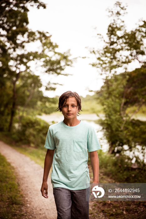 Boy (8-9) walking on dirt road trees in background