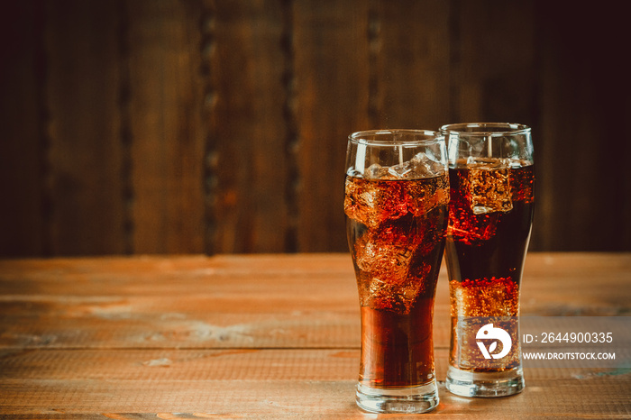 Beautiful cold fizzy cola soda with cubes ice in glasses goblet on old wooden background with free space