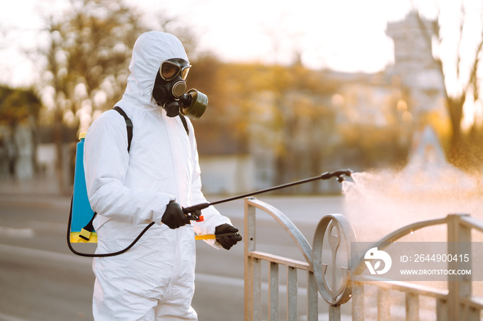 A man wearing special protective disinfection suit sprays sterilizer  in the empty public place at dawn in the city of quarantine. Covid -19. Cleaning concept.