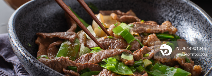 eating chinese beef and snowpeas stirfry in bowl with chopsticks