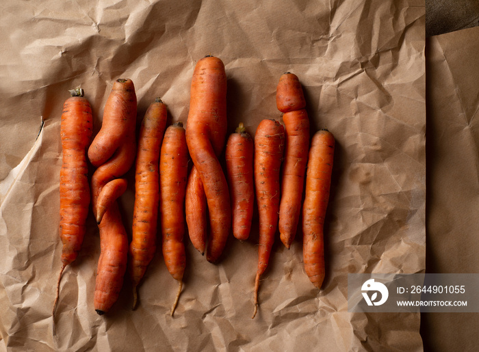 Lot of crooked carrots on craft paper. Organic ugly carrots. The concept of veganism and sustainable nutrition. Top view