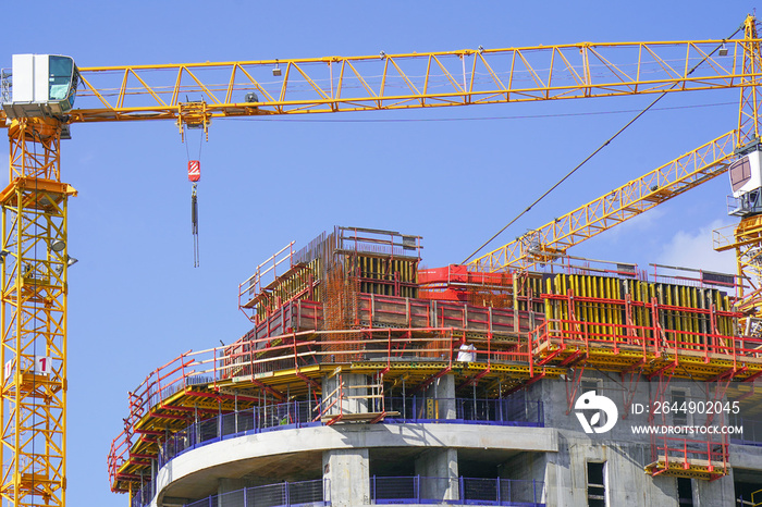 Construction site with cranes and a building against a blue sky.