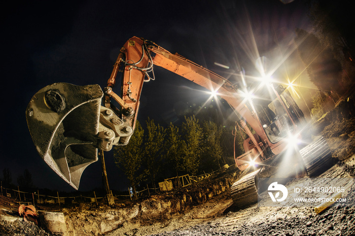 Orange excavator digger working at night on the street