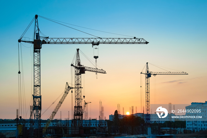 Industrial landscape with silhouettes of constraction cranes on sunset background