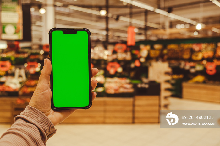 Mobile phone Chroma key. Close up of woman hand holds smart phone with green screen at shopping mall store. Buying food at supermarket, grocery shop center online. Department store. Gadgets