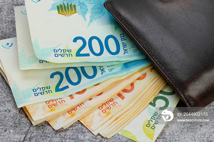 200 and 100 Israeli shekels banknotes stick out of a leather wallet close-up.