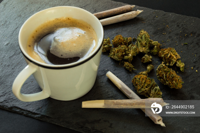 Delicious cup of coffee, a pile of high quality marijuana buds with some cigars of weed ready to smoke. Top view with background of black stone.