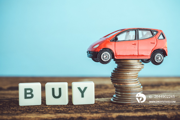 Word BUY and miniature red car model with stacked coins on wooden table with copy space. Business, finance or budget plan money saving for buying a new car and auto insurance concept.