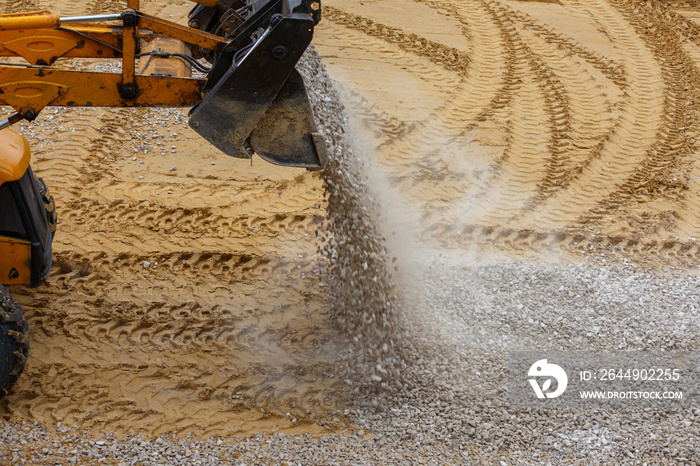 a bulldozer pours gravel from a bucket onto the compacted sand at a construction site