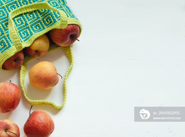 Modern blue yellow crochet bag for shopping with fresh red apples. Colored crochet bag with ethnic geometric pattern. Sustainable, reusable bag. Copy space.