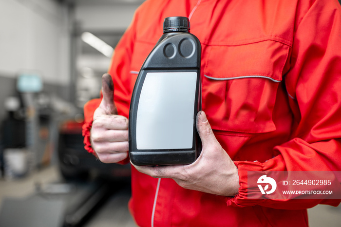 Auto mechanic in red uniform holding bottle with engine oil at the car service, close-up view with no face