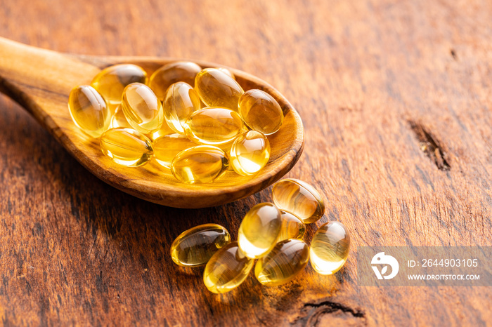 Fish oil capsules. Yellow omega 3 pills in spoon on wooden table.