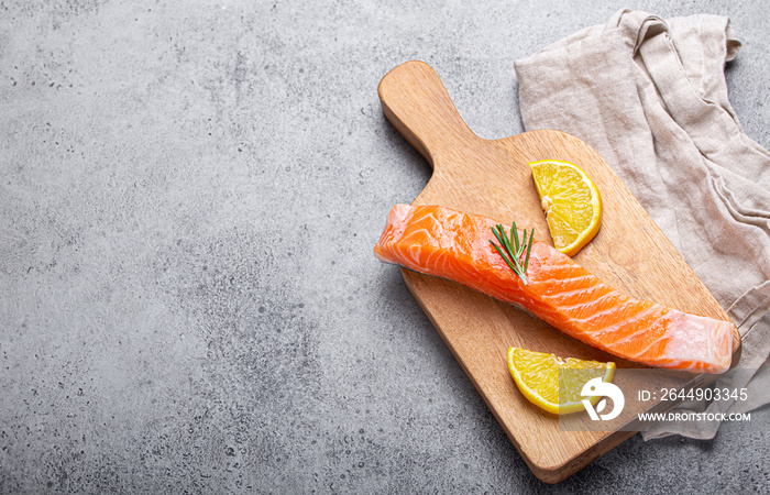 Raw salmon fish fillet with lemon wedges and rosemary on wooden cutting board on gray stone concrete rustic background kitchen table from above, healthy eating and diet