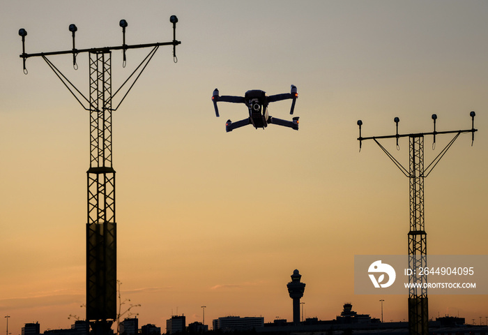 Unmanned drone flying near runway at airport in between approaching runway lighting at sunset