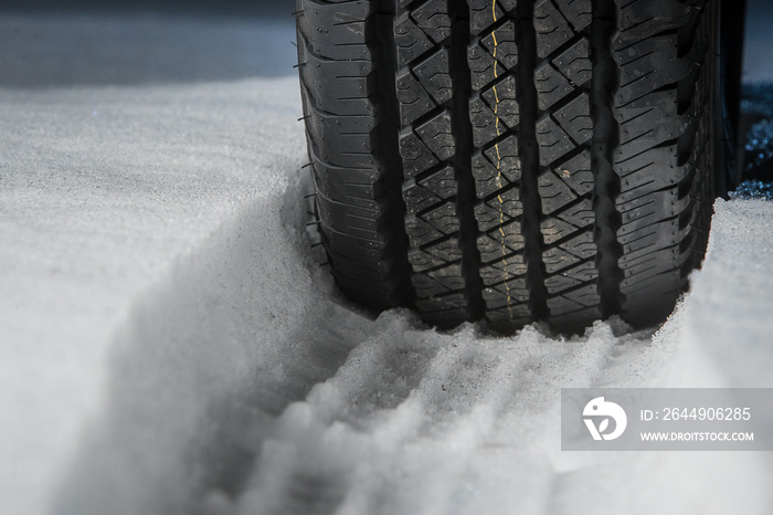 All terrain tire in snow. Snow track visible in snow with a rubber car or SUV tire in front. Tread marks in snow. Winter road safety concept.