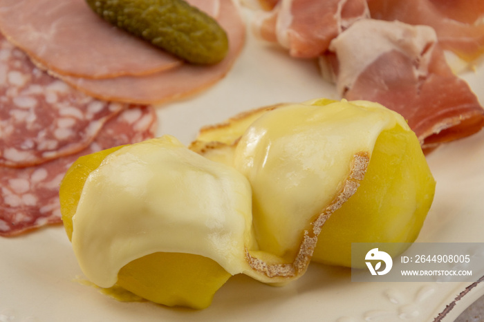 fromage à raclette fondu sur des pommes de terre et charcuterie dans une assiette