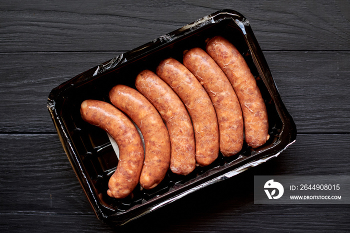 Raw grilled sausages in the package on a dark wooden background.