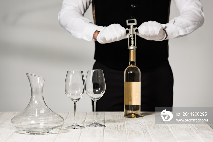 partial view of waiter in white gloves opening bottle of wine with corkscrew