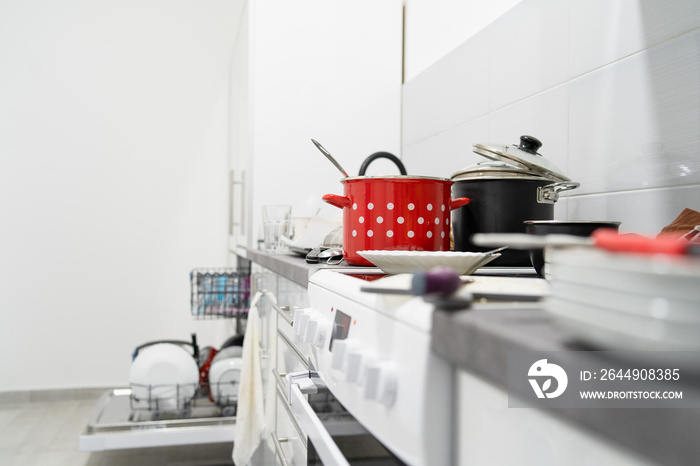 Side view on white kitchen with unwashed dirty pots and dishes on the countertop utensils and kitchen appliances in a mess after cooking