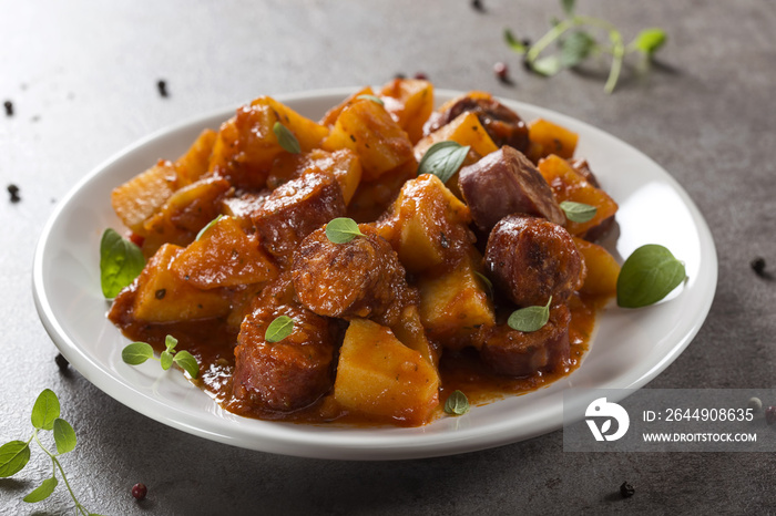 Potatoes stew with pork sausage slices and tomato sauce on a white plate