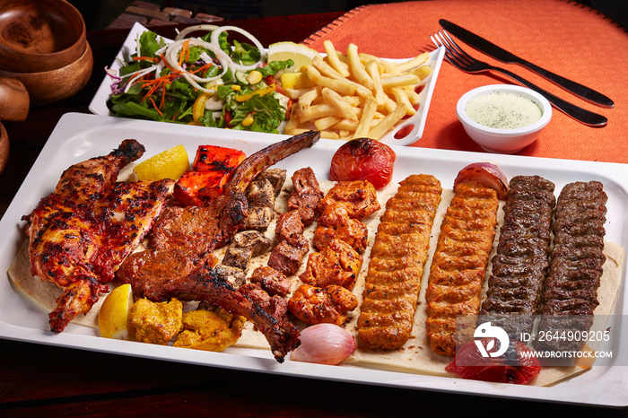 Spicy bbq Mixed Grills platter with tikka boti kababs, fries, salad and raita served in dish isolated on table side view of middle east food