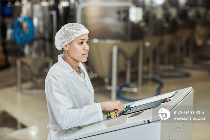 Female worker wearing lab coat using control panel at food factory