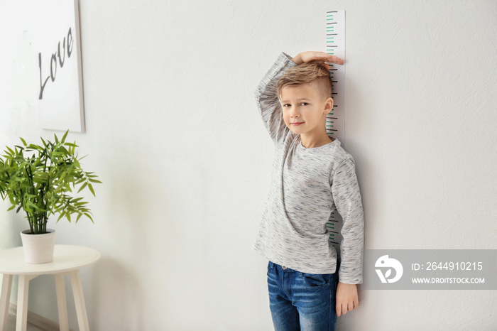 Cute little boy measuring height near wall at home