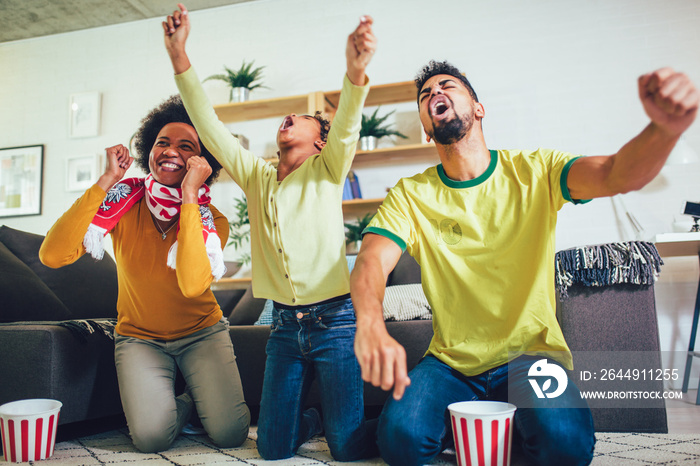 Happy African American family of three watching tv and cheering sport games on sofa at home