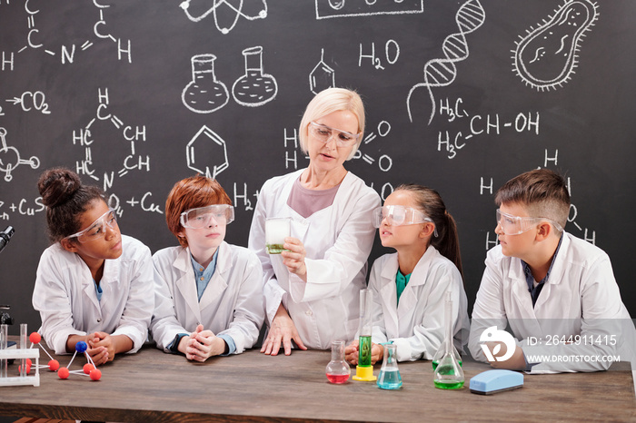 Young teacher of chemistry and group of pupils discussing chemical reaction