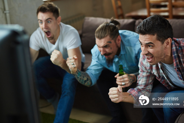 Portrait of three emotional adult men watching sport match on TV screaming and cheering  with excitement while sitting on couch in living room with beer