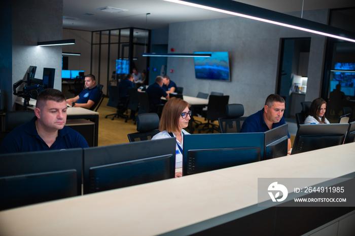 Group of Security data center operators (administrators) working in a group at a CCTV monitoring room while looking at multiple monitors ( computer screens)