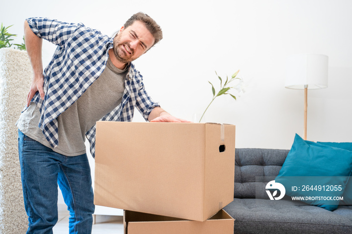 Pain in back. Young man suffering while lifting a cardboard box