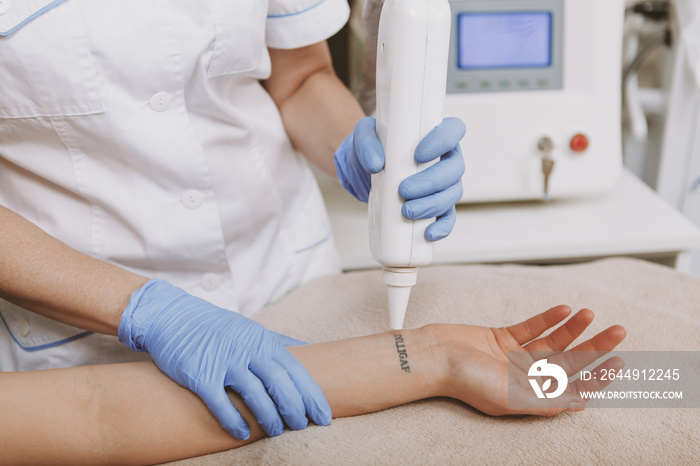 Cropped shot of unrecognizable woman getting tattoo removed by laser at beauty salon. Professional dermatologist using laser; removing tattoo on the skin of female client